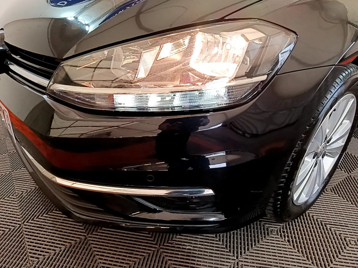 Gros plan sur l'avant droit noir d'une Volkswagen Golf 2018, mettant en valeur le phare allumé et la jante alliage.