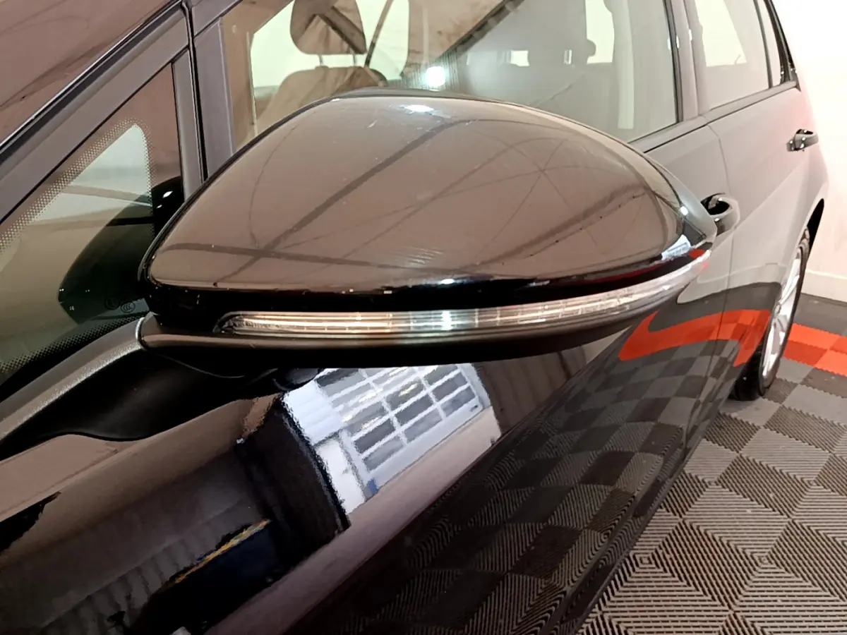 Gros plan sur le rétroviseur côté gauche noir brillant de la Volkswagen Golf 1.6 TDI 2018 avec clignotant intégré.