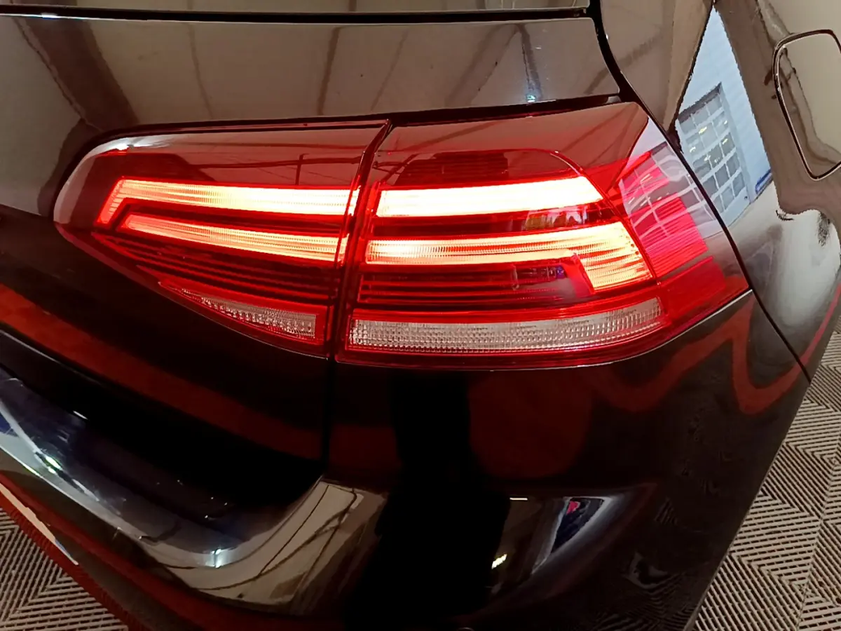 Gros plan sur le feu arrière droit allumé d'une Volkswagen Golf noire, reflétant l'environnement intérieur.