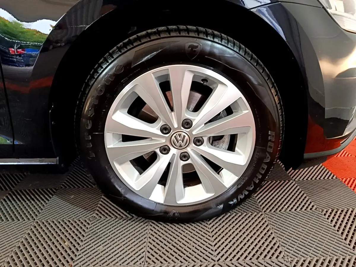 Gros plan sur la roue avant droite d'une Volkswagen Golf noire, avec jante argentée et logo VW central.