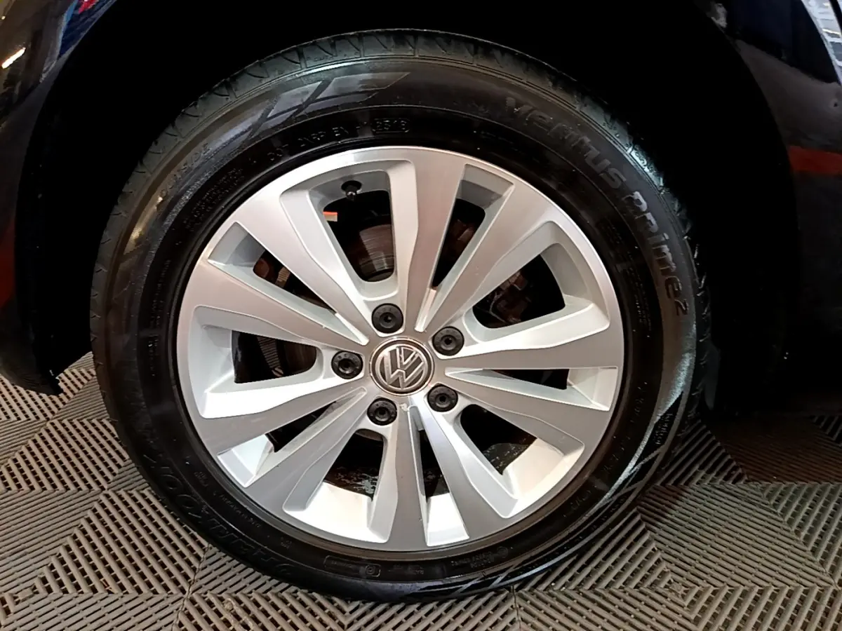 Gros plan sur la roue avant droite de la Volkswagen Golf noire, jante alliage argentée avec logo VW au centre.