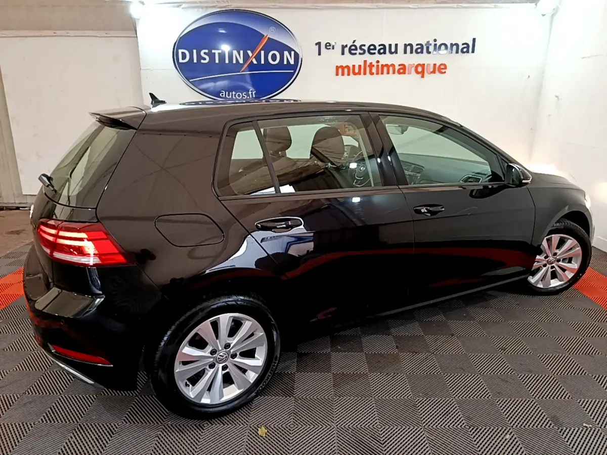 Vue 3/4 arrière droite d'une Volkswagen Golf noire 2018 avec feux arrière allumés dans un showroom.