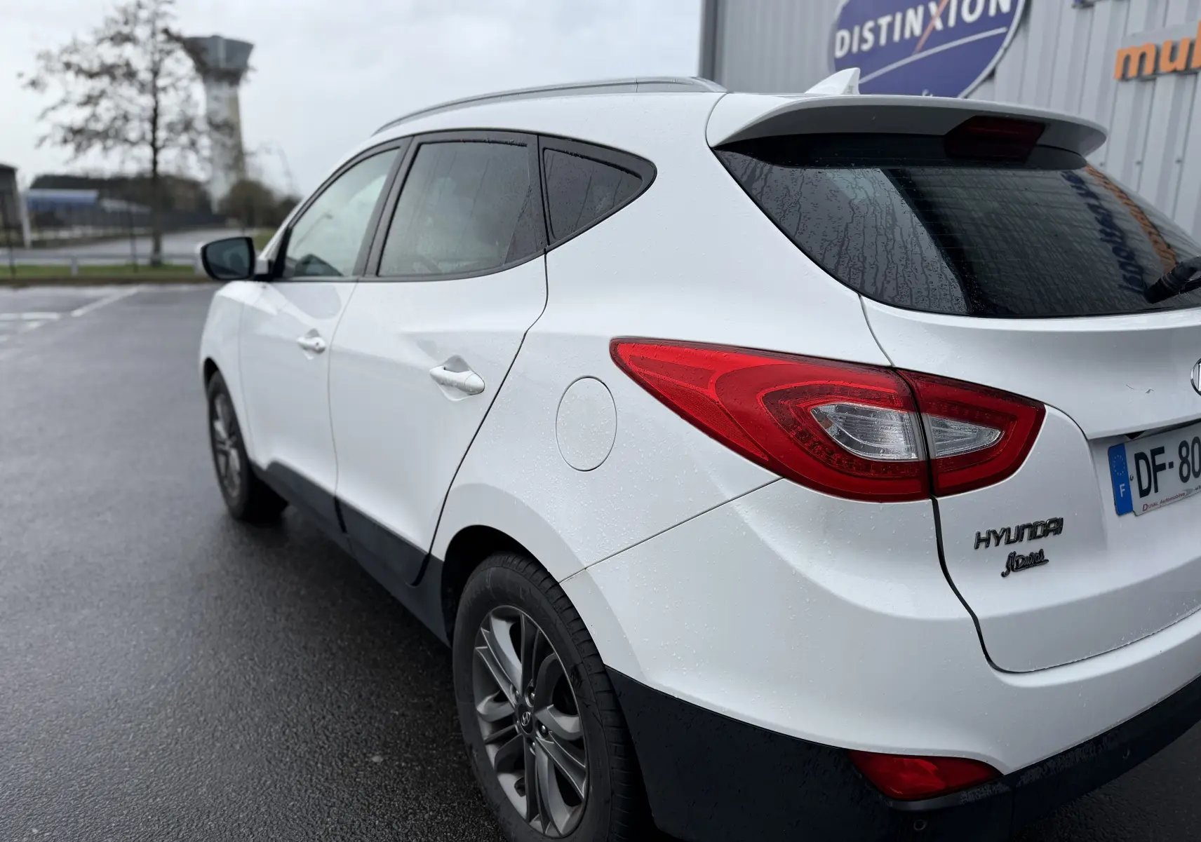 Vue 3/4 arrière droite d'un Hyundai ix35 blanc 2014 avec feux arrière rouges et jantes alliage foncé.