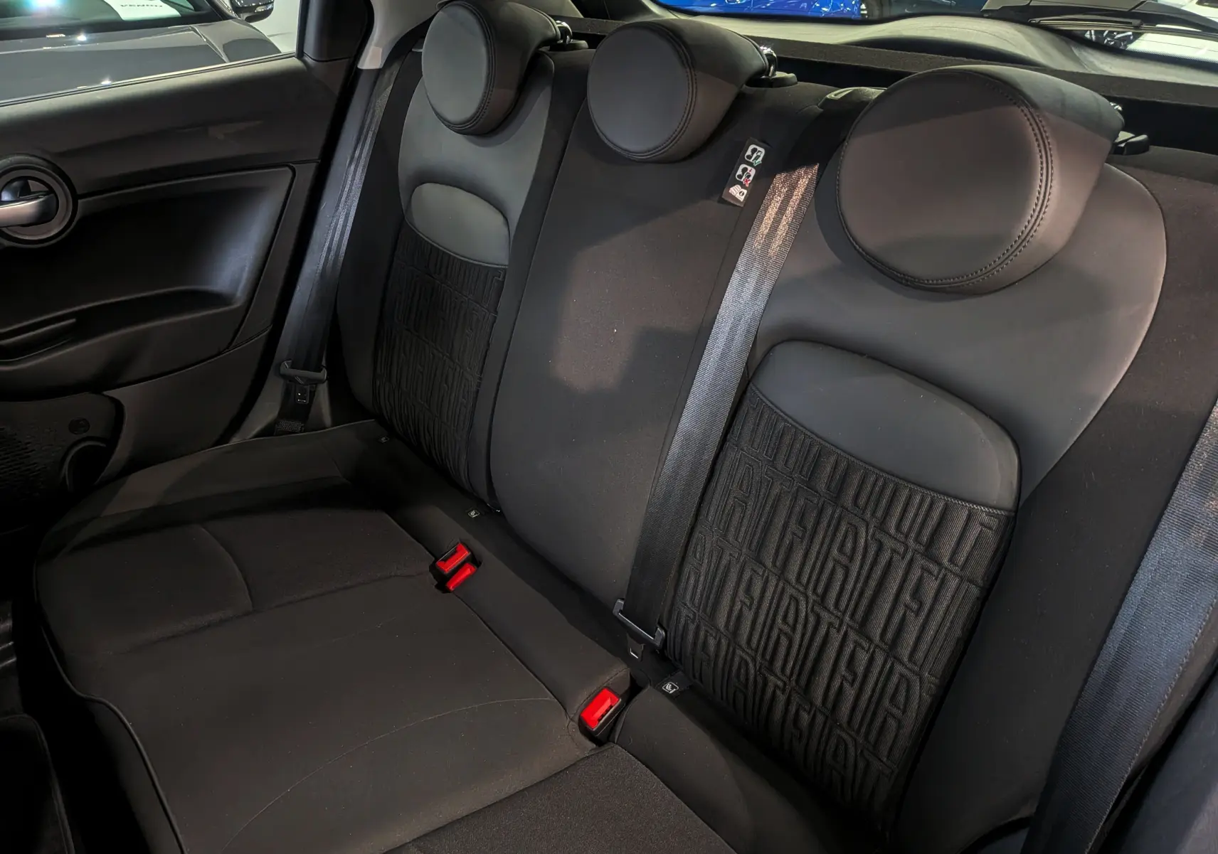 Vue intérieure des sièges arrière noirs de la FIAT 500X 2024, avec motifs FIAT sur les dossiers et ceintures visibles.