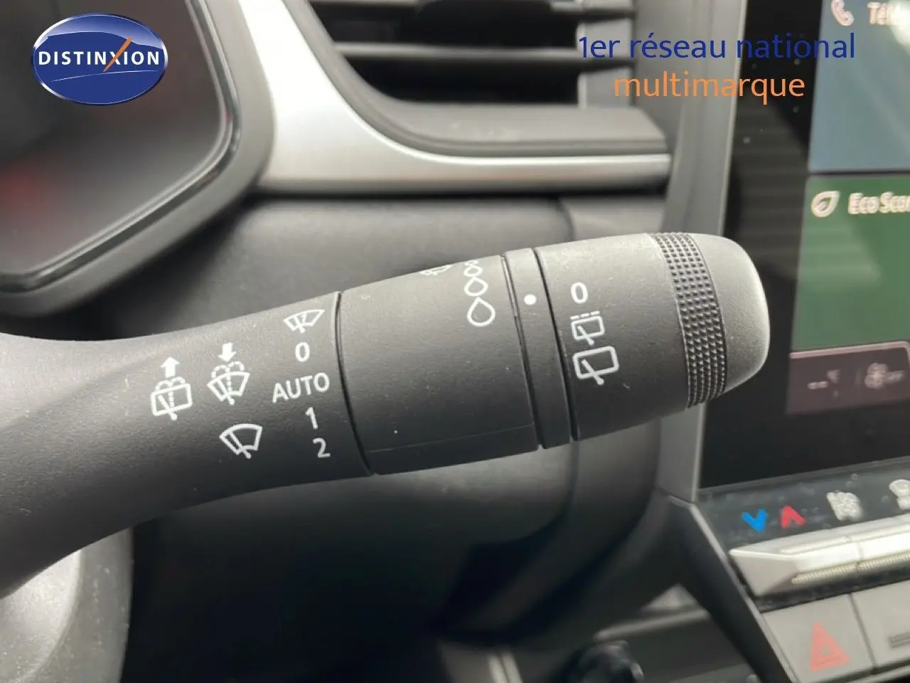 Gros plan sur la commande d’essuie-glace du Renault Symbioz blanc nacré, avec tableau de bord et écran tactile en arrière-plan.
