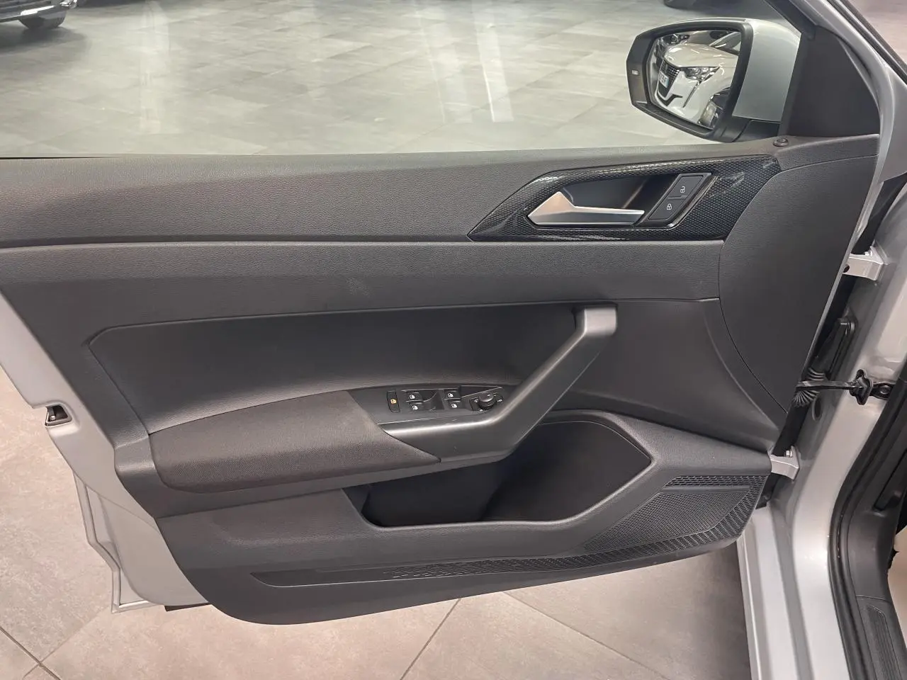 Vue intérieure côté gauche de la porte avant gris clair d'une Volkswagen Polo 2024 avec commandes de vitres et rétroviseur.
