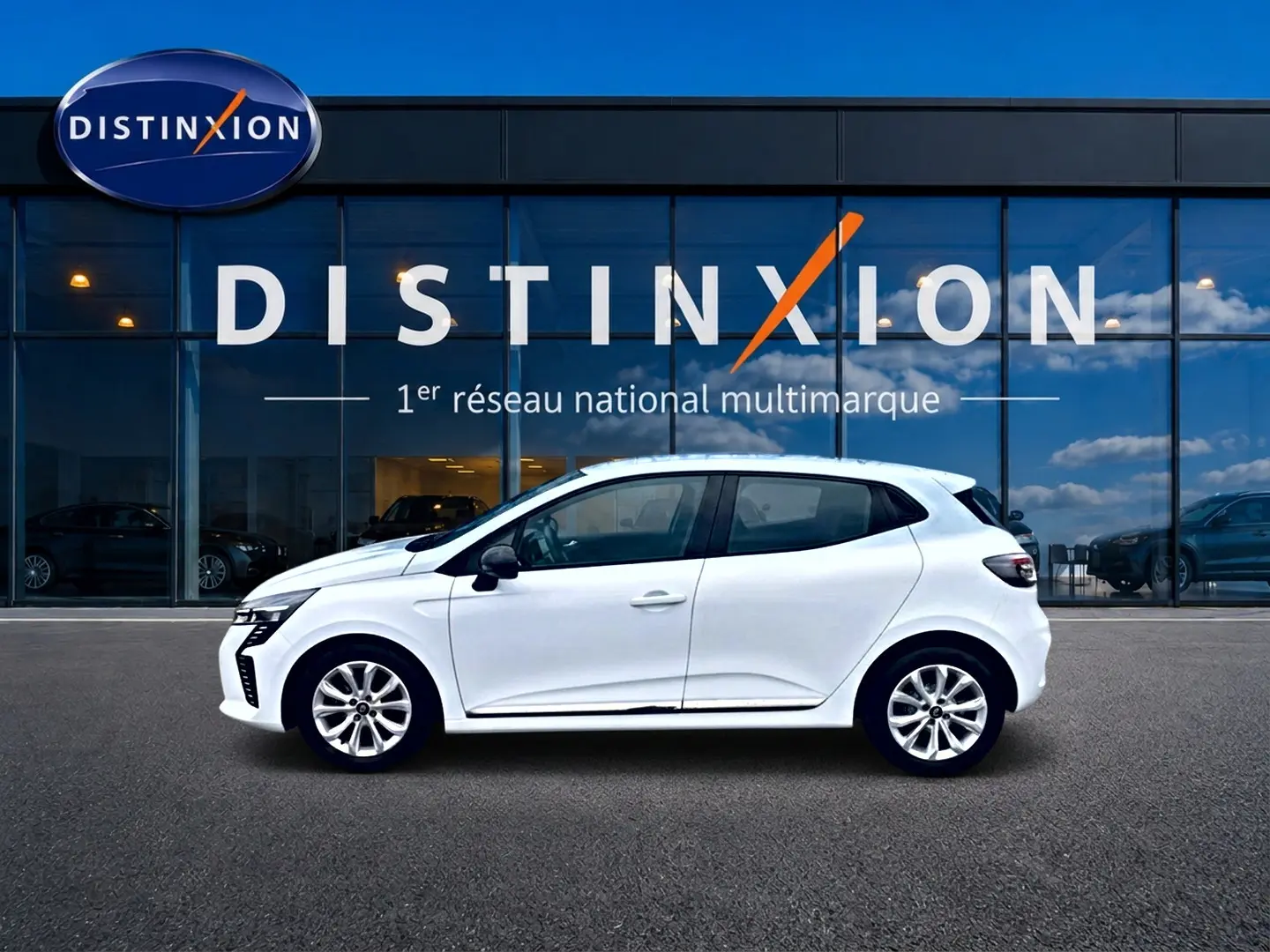 Profil droit d'une Renault Clio V blanche 2025, avec jantes alliage et poignées ton carrosserie, devant une vitrine Distinxion.
