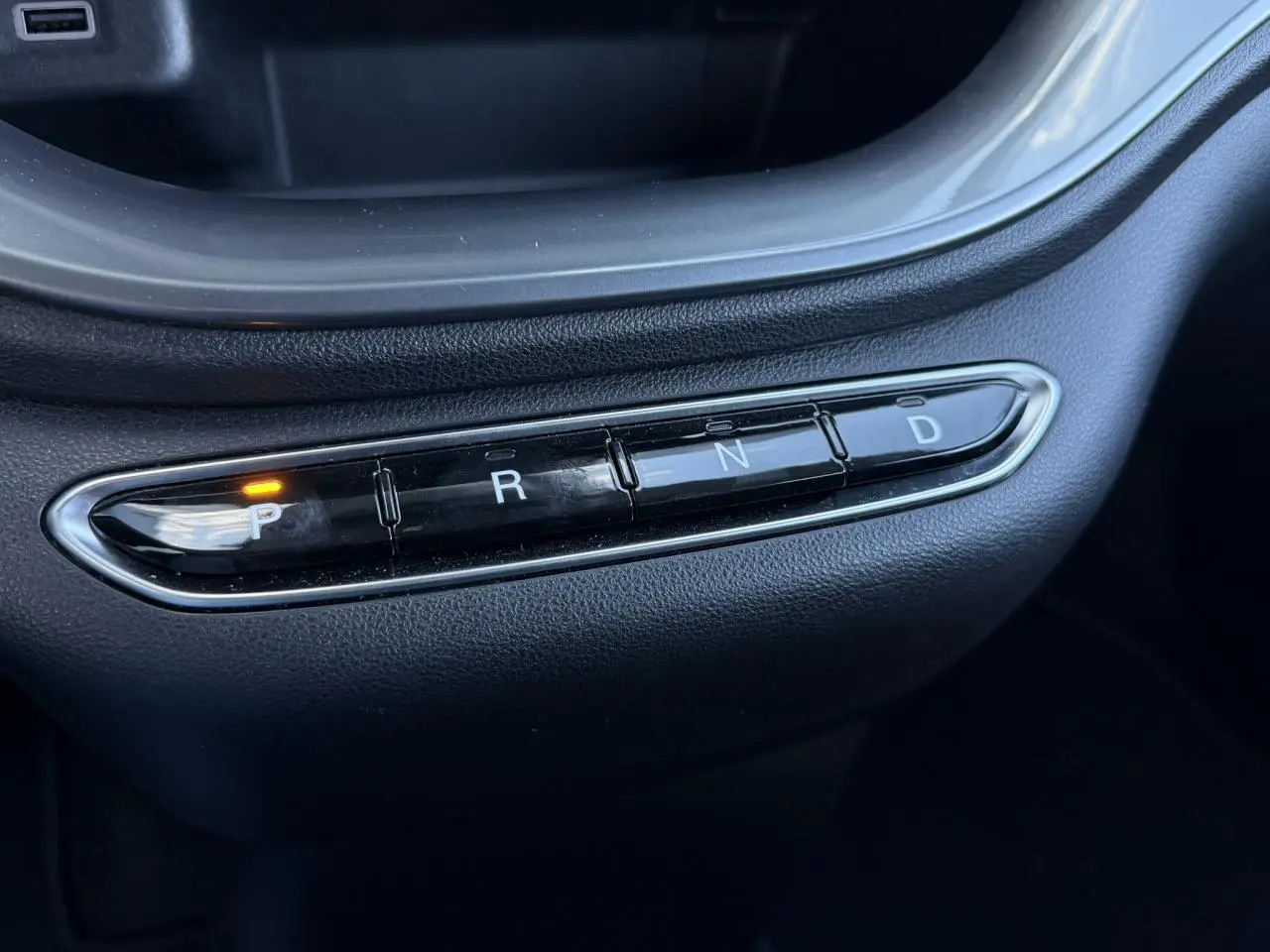 Gros plan sur la console centrale noire de la Fiat 500 électrique 2024 avec sélecteur de boîte auto et témoin de parking allumé.