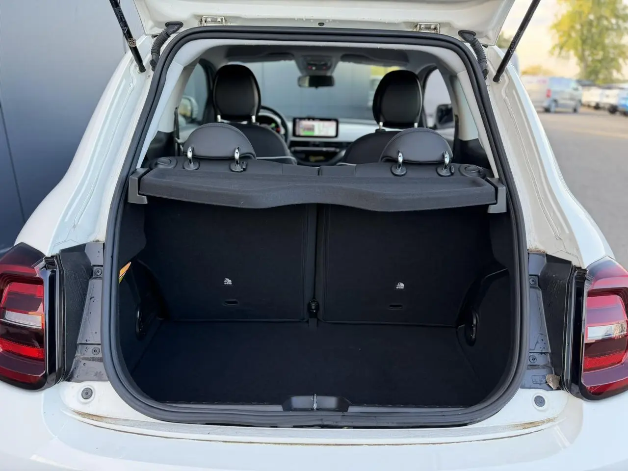 Coffre ouvert vu de l'arrière d'une Fiat 500 électrique blanc Arctic, banquette arrière et intérieur noir visibles.