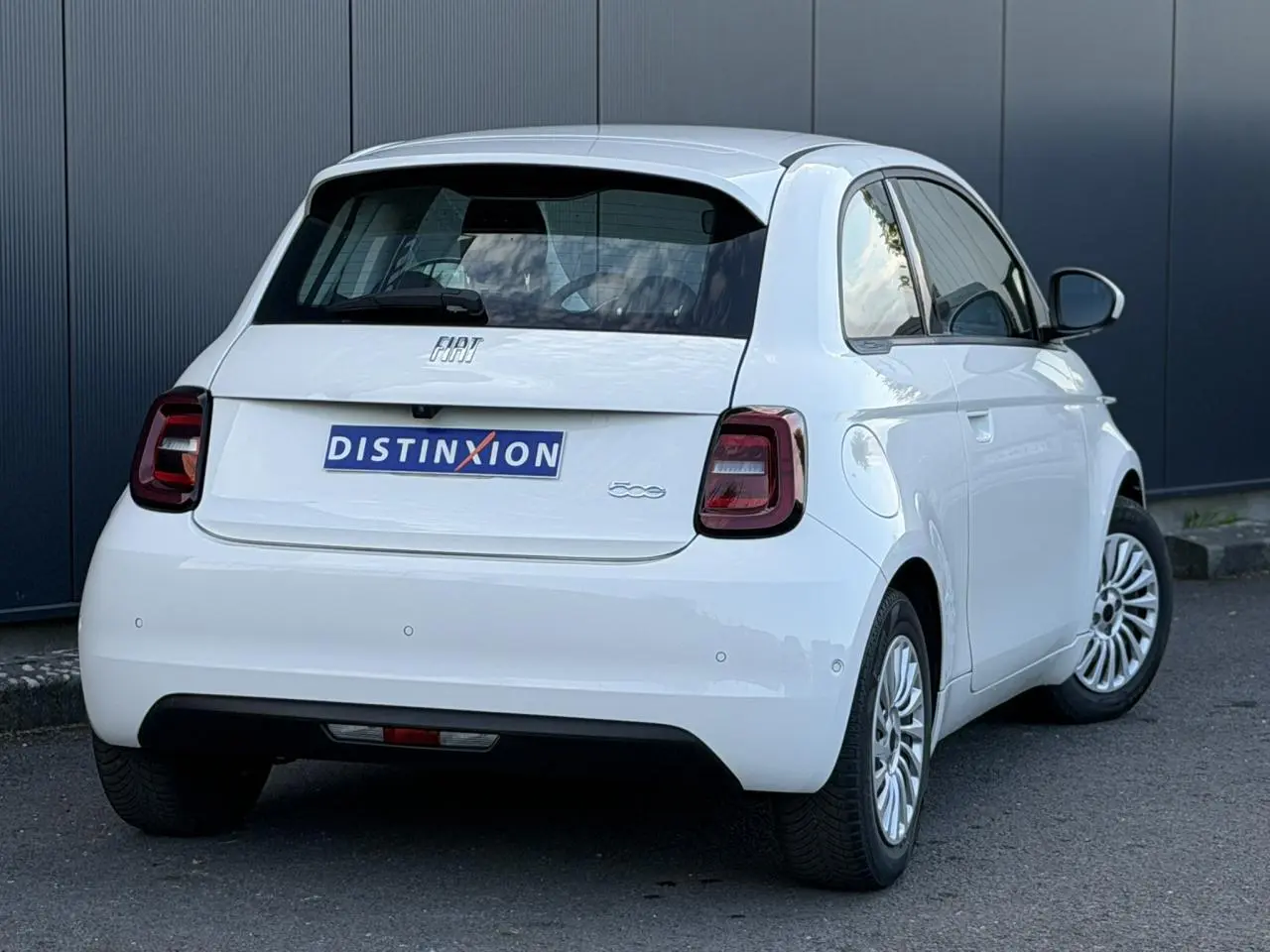 Vue 3/4 arrière droite d'une Fiat 500 électrique blanc Artic avec feux arrière foncés et jantes alliage multibranches.