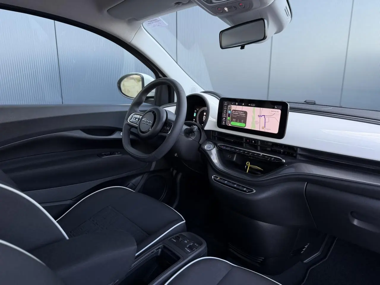 Vue intérieure côté conducteur de la Fiat 500 électrique 2024 avec tableau de bord blanc Artic et écran tactile central.