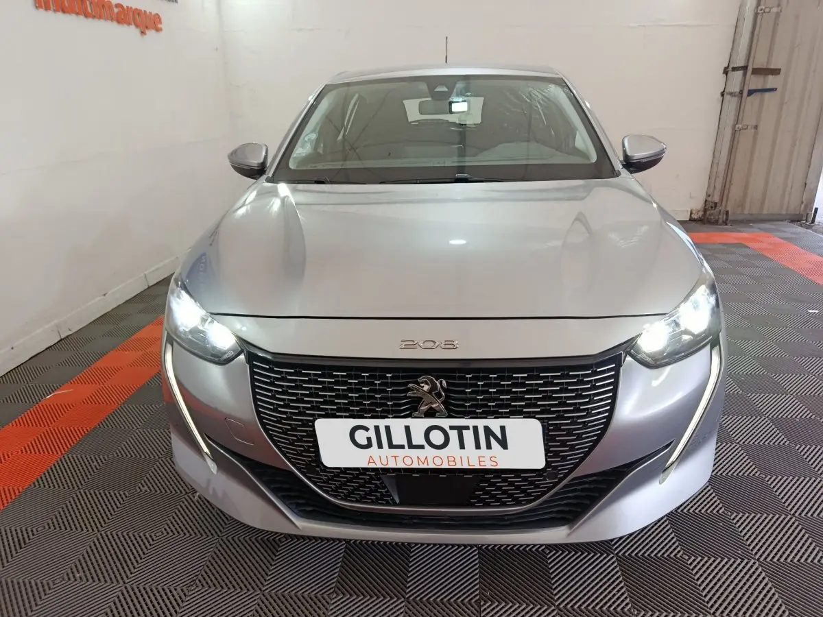 Vue frontale d'une Peugeot 208 électrique gris clair avec phares LED allumés et calandre noire distinctive.