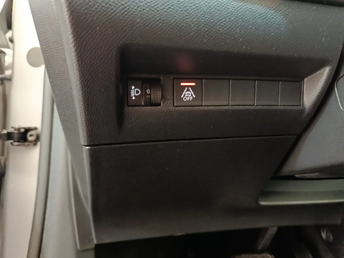 Gros plan sur les commandes de réglage des phares et désactivation de l'aide au maintien de voie dans une Peugeot 208 gris clair électrique.