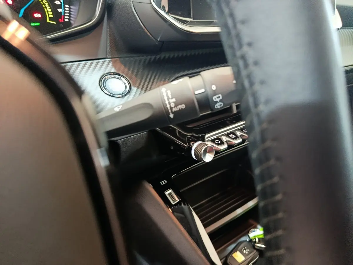 Détail intérieur côté conducteur du tableau de bord noir avec bouton démarrage et commandes Peugeot 208 électrique gris clair.