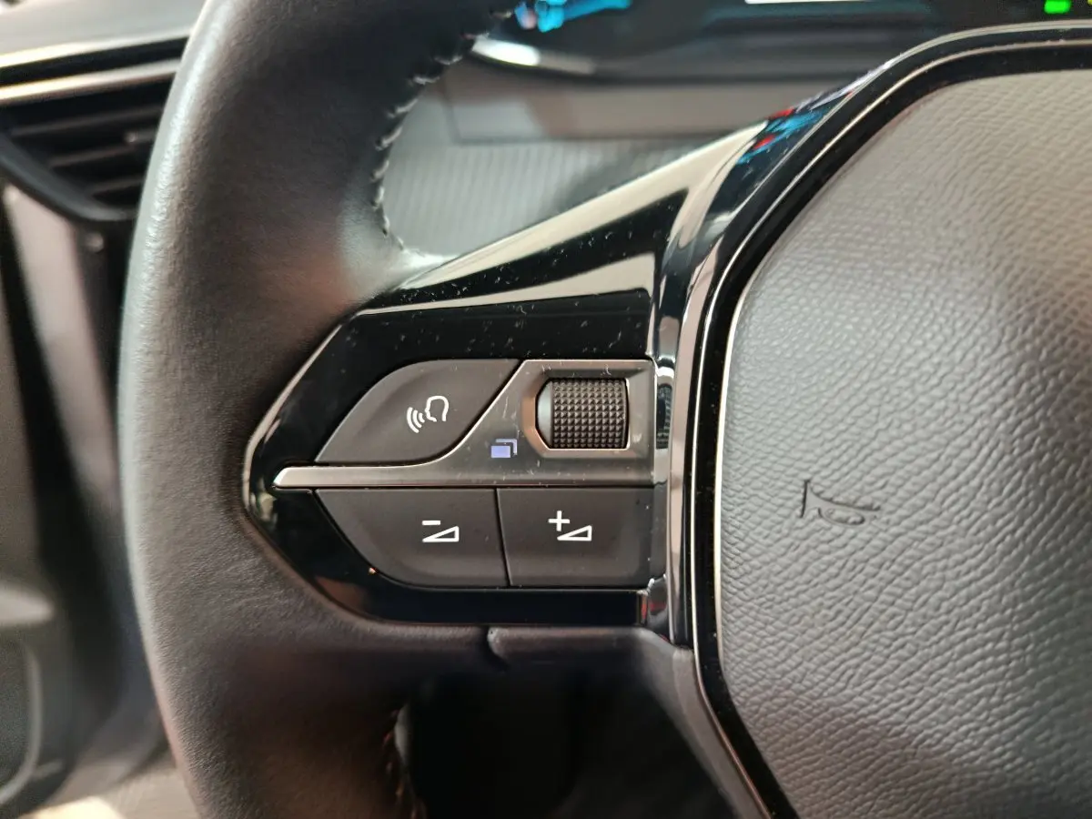 Gros plan sur les commandes du volant cuir noir du Peugeot 208 électrique Active Business gris clair, côté gauche.
