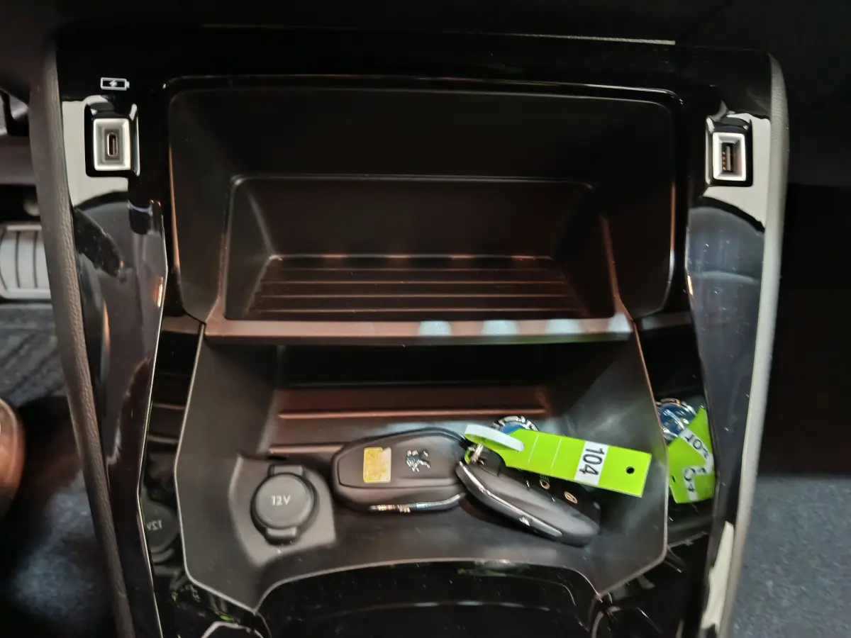 Rangement central noir avec clés Peugeot et prise 12V visible dans l'habitacle d'une 208 électrique gris clair.