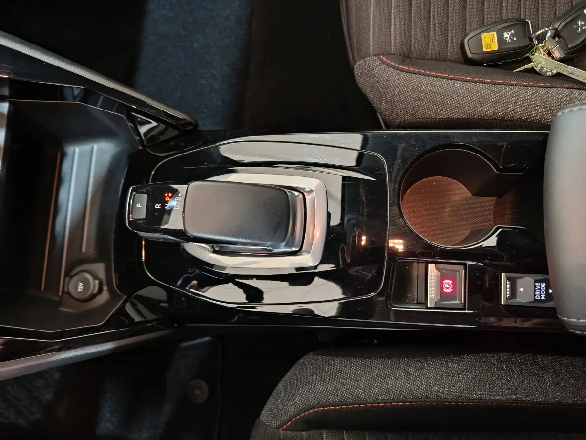 Vue rapprochée de la console centrale noire brillante avec levier de boîte auto et bouton frein à main électrique d’une Peugeot 208 Electrique Active Business.