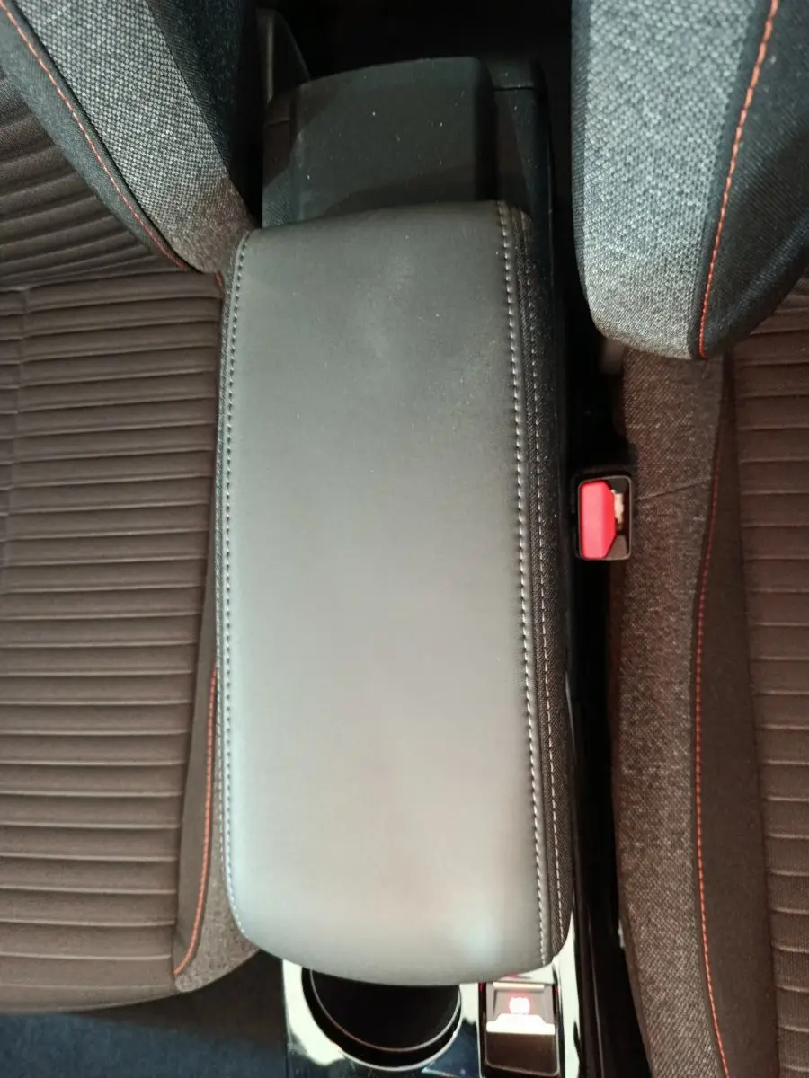 Vue plongeante sur l'accoudoir noir entre les sièges gris foncé avec surpiqûres rouges du Peugeot 208 Electrique Active Business.