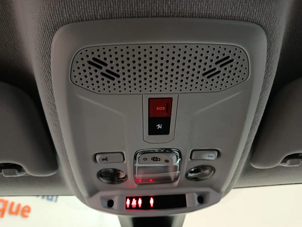 Vue en contre-plongée du plafonnier gris clair de la Peugeot 208 électrique avec bouton SOS rouge et éclairages intégrés.
