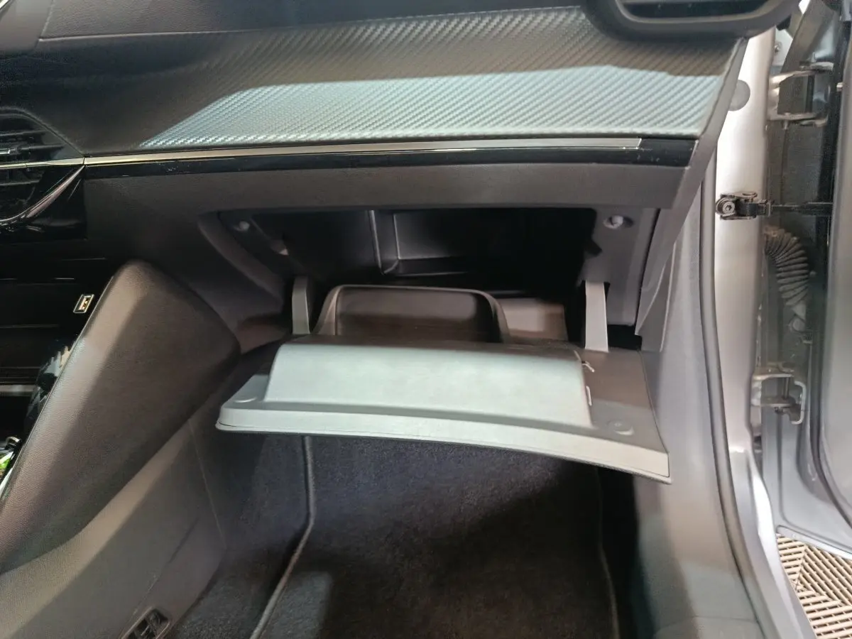 Vue intérieure côté passager de la Peugeot 208 électrique gris clair, montrant la boîte à gants ouverte et le tableau de bord.