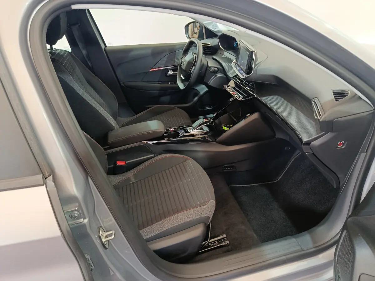 Intérieur côté conducteur de la Peugeot 208 électrique gris clair, avec tableau de bord moderne et écran tactile central.