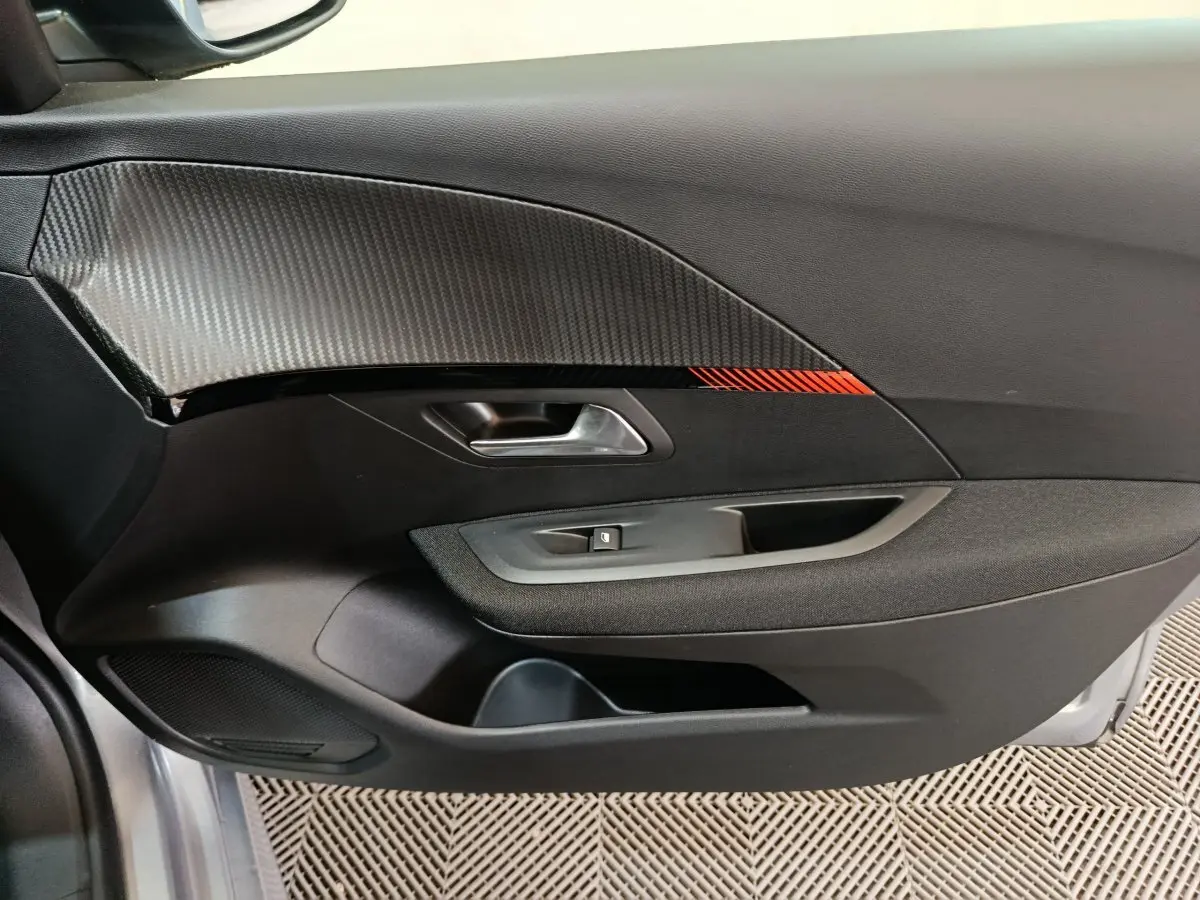 Vue rapprochée de la porte côté gauche de la Peugeot 208 électrique gris clair avec insert carbone et détail rouge.