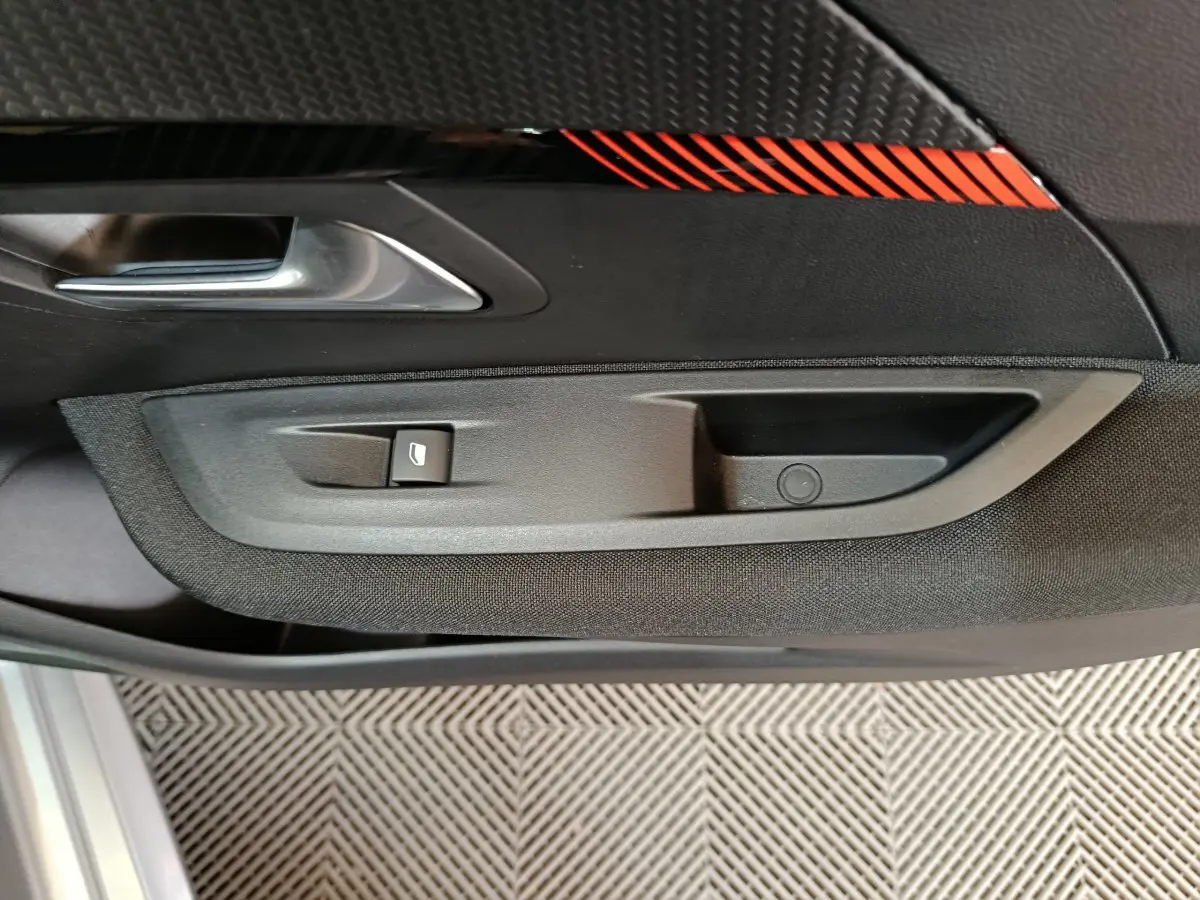Poignée intérieure côté gauche avec bouton de lève-vitre sur la porte noire et décor rouge de la Peugeot 208 électrique 2020.
