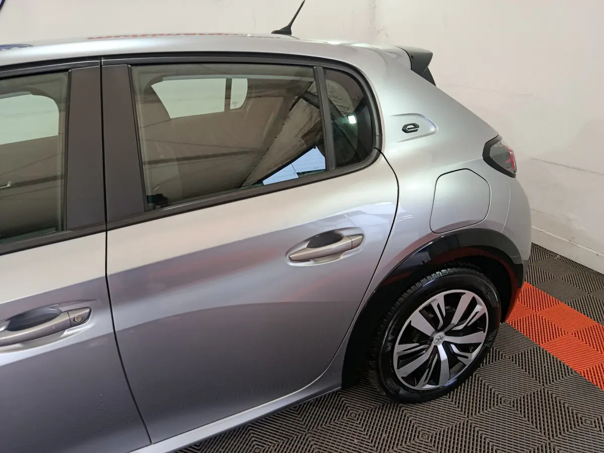 Vue côté droit arrière d'une Peugeot 208 électrique gris clair avec logo "e" distinctif près de la vitre arrière.