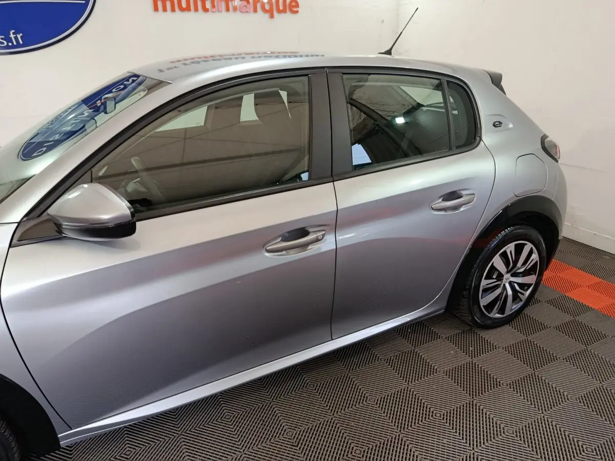 Profil côté gauche d'une Peugeot 208 électrique Active Business gris clair, avec jantes alliage et rétroviseur assorti.