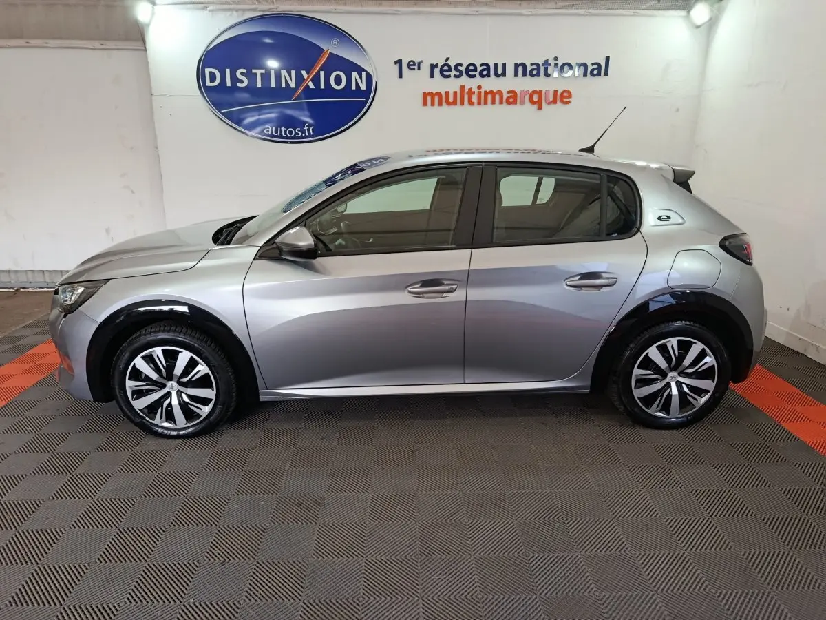 Peugeot 208 électrique gris clair vue de profil côté gauche, avec jantes stylisées et logo "e" de la version électrique.