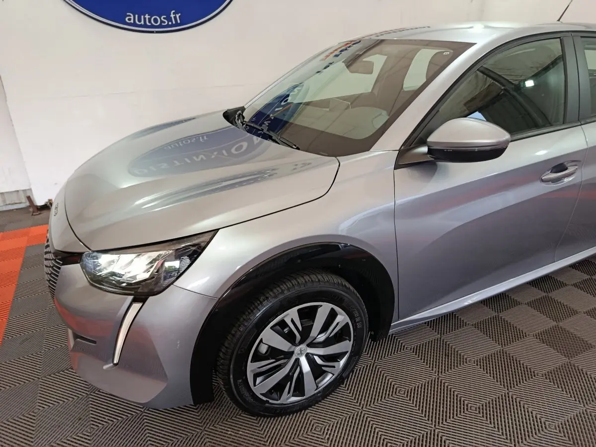 Vue 3/4 avant droit d'une Peugeot 208 électrique Active Business gris clair avec phares LED et jantes stylisées.