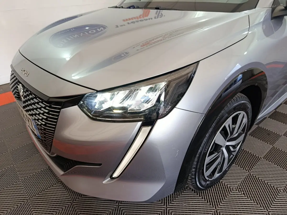 Vue 3/4 avant droit d'une Peugeot 208 électrique gris clair avec feux LED et jante spécifique Active Business.