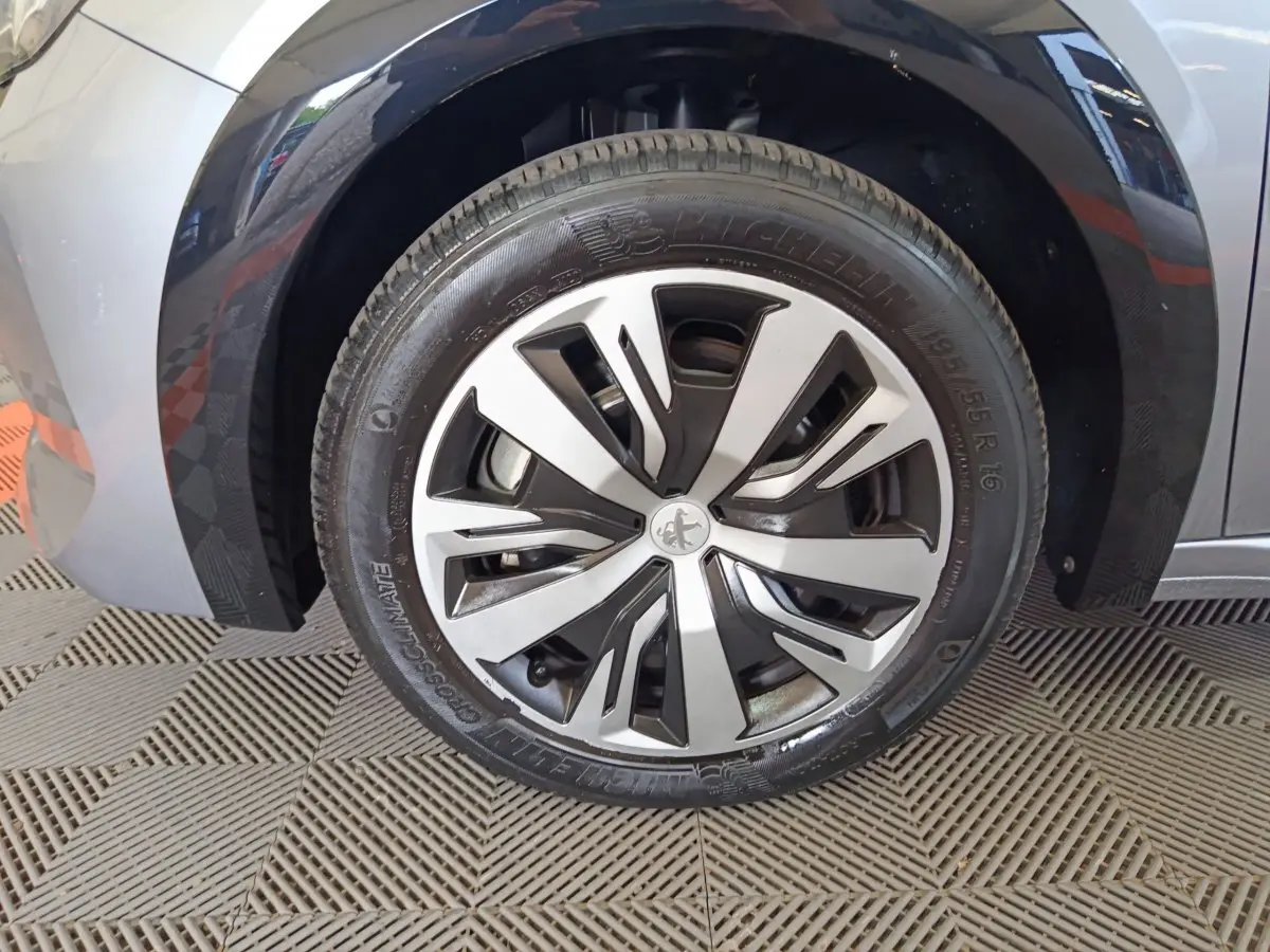 Gros plan sur la roue avant gauche gris clair d'une Peugeot 208 Electrique Active Business avec jante design Peugeot.
