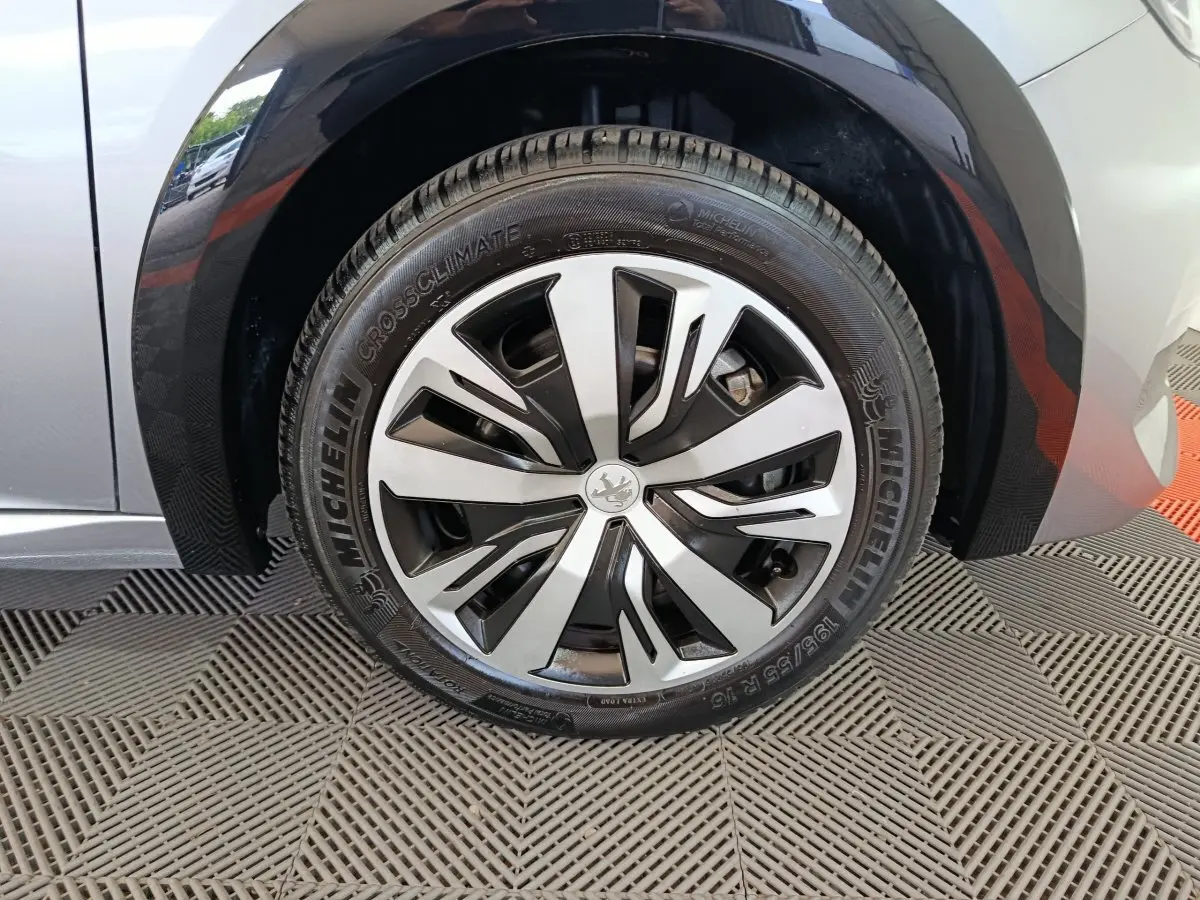 Gros plan sur la roue avant droite de la Peugeot 208 électrique gris clair avec jante alliage au design moderne.