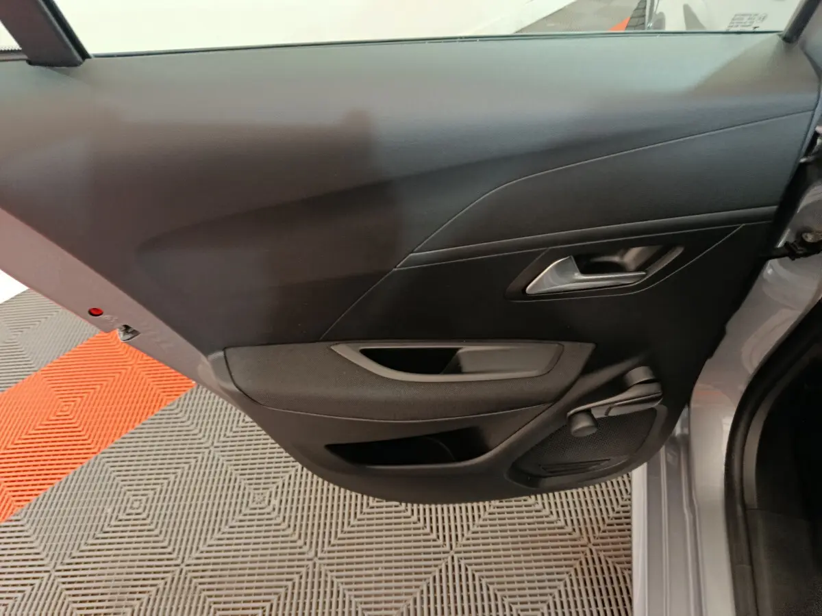 Vue intérieure de la porte arrière droite noire d'une Peugeot 208 électrique gris clair, avec poignée et haut-parleur intégrés.