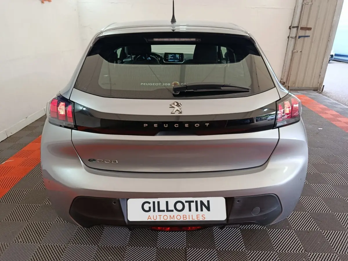 Vue arrière d'une Peugeot 208 électrique gris clair avec feux LED et logo lion sur hayon noir brillant.