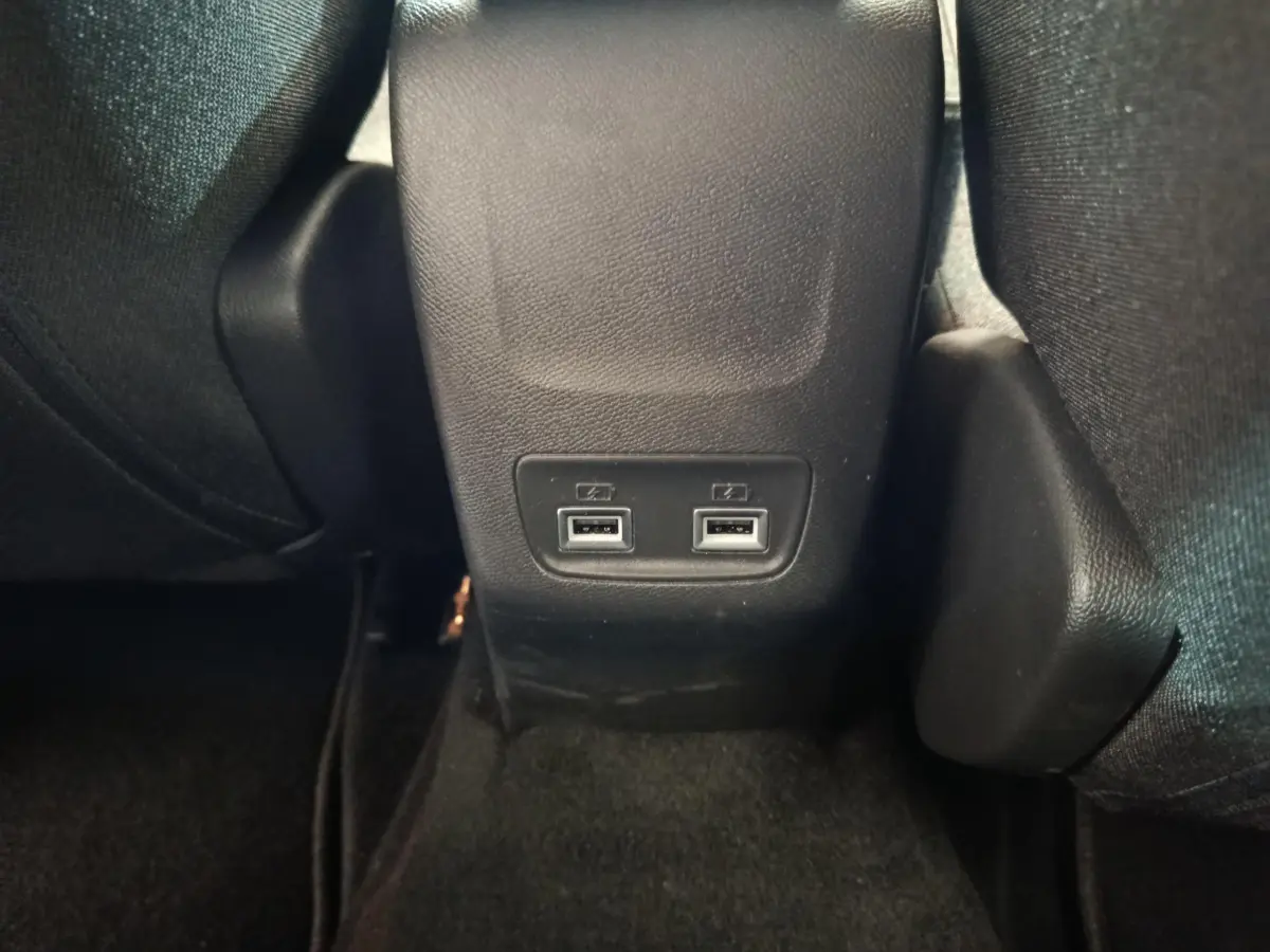 Prise double USB arrière au sol entre les sièges noirs de la Peugeot 208 électrique gris clair.