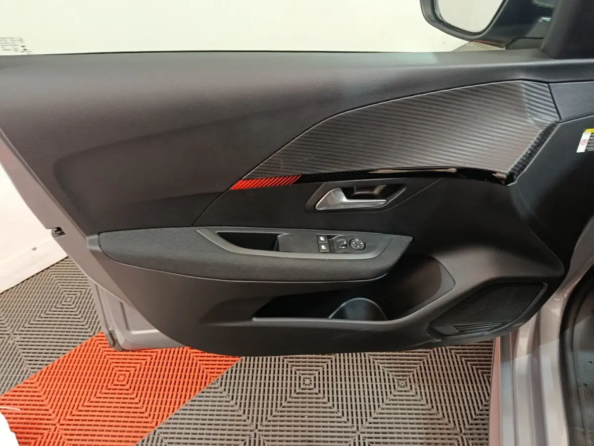 Vue intérieure côté gauche de la porte d'une Peugeot 208 électrique gris clair avec insert décoratif noir et rouge.