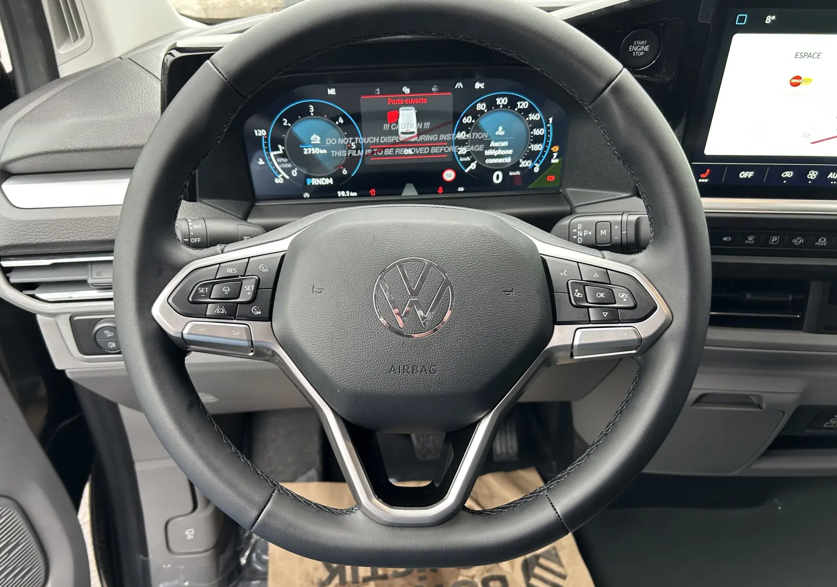 Vue rapprochée du volant multifonction noir du Volkswagen Transporter T7 avec tableau de bord digital et écran tactile.