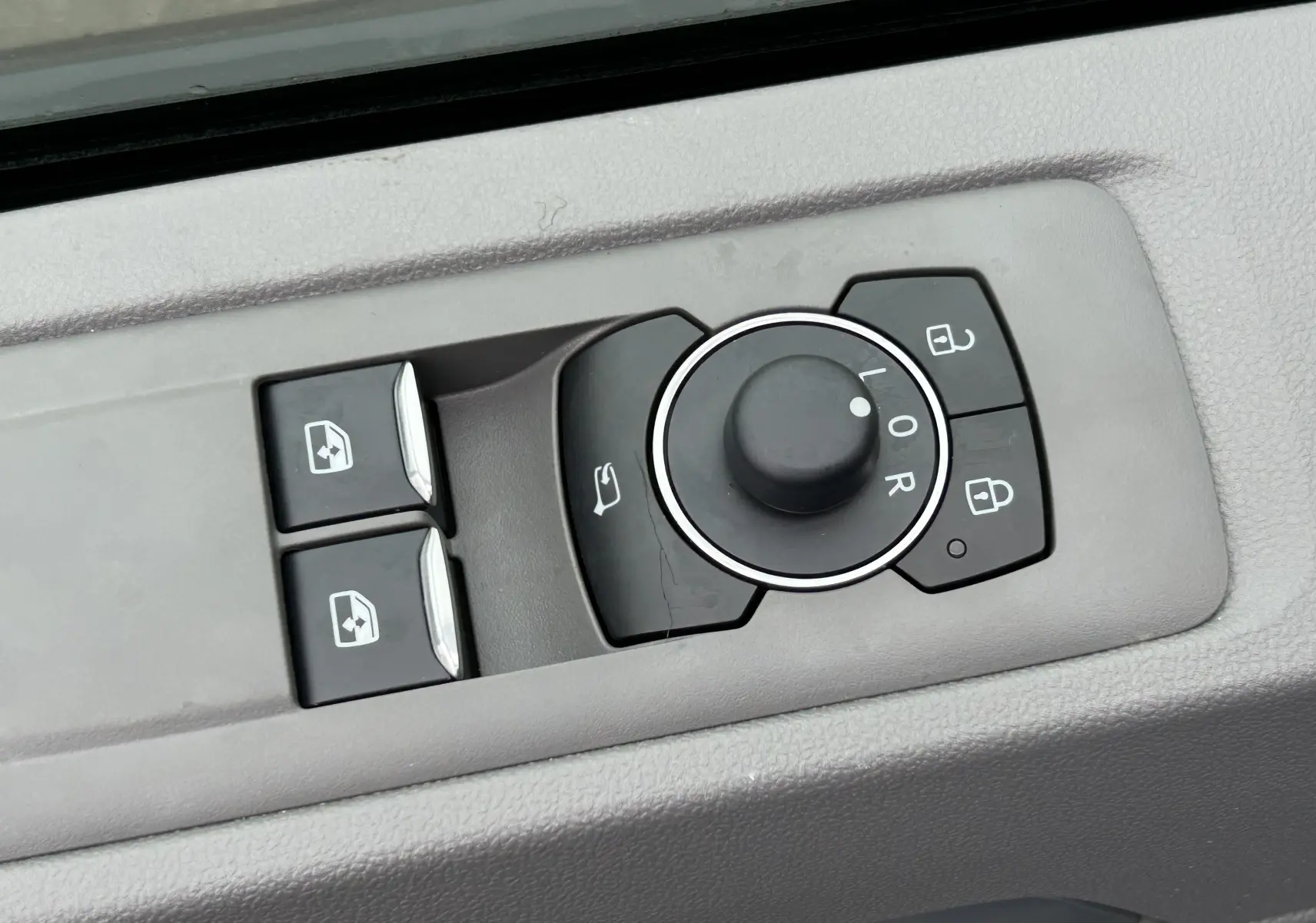 Gros plan sur les commandes de réglage des rétroviseurs et des vitres côté conducteur du Volkswagen Transporter T7 Business gris Graphite Dust.