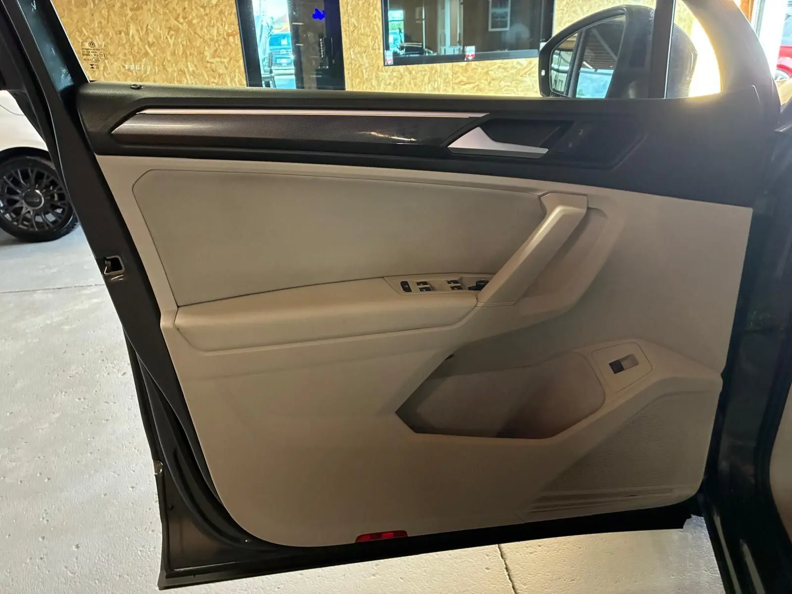 Vue intérieure côté gauche de la porte avant d’un Volkswagen Tiguan gris, avec commandes de vitres et garniture beige.