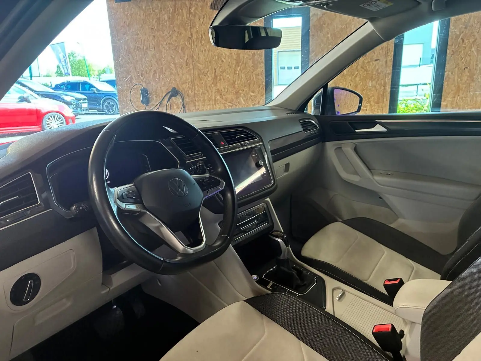 Vue intérieure côté conducteur du Volkswagen Tiguan 2023, volant cuir multifonctions et sièges tissu clair et noir.