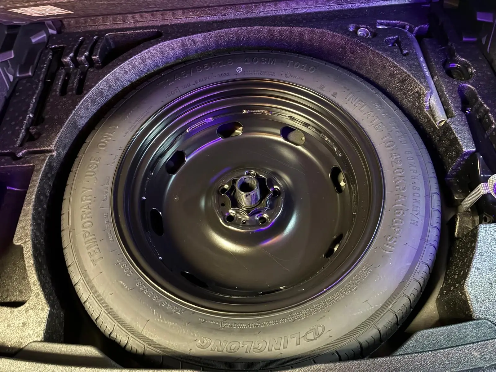 Gros plan sur la roue de secours noire dans le coffre du Volkswagen Tiguan gris 2023, détail du pneu temporaire.