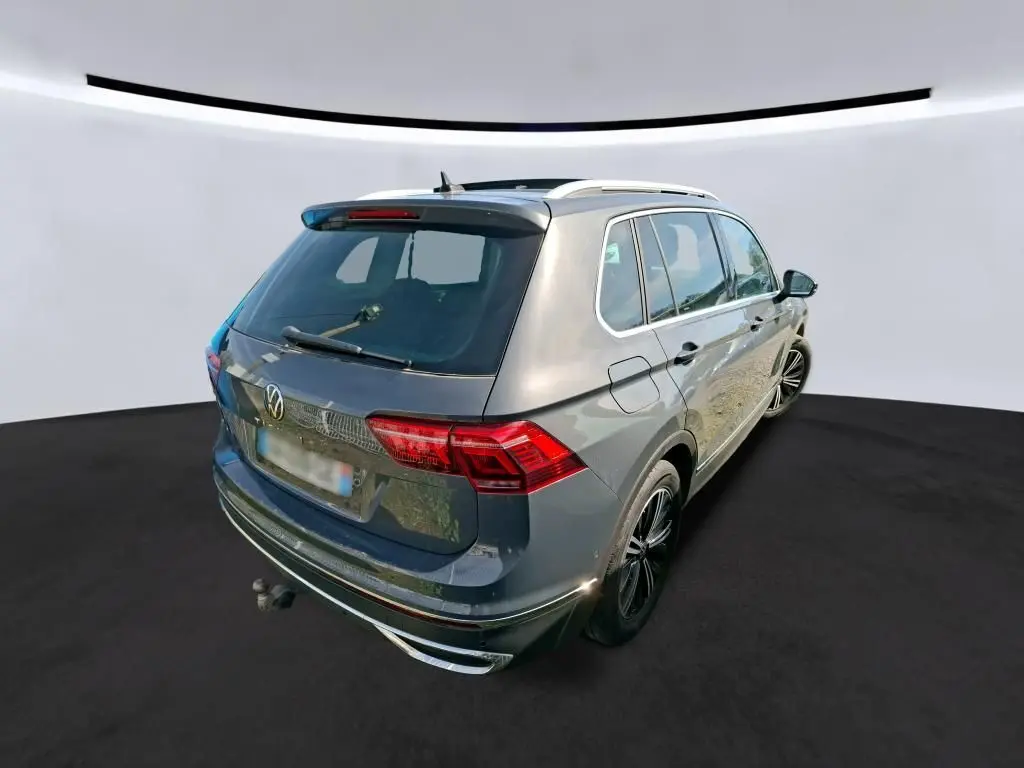Vue de profil côté droit d'un Volkswagen Tiguan gris 2023 avec jantes noires et toit ouvrant en intérieur d'atelier.