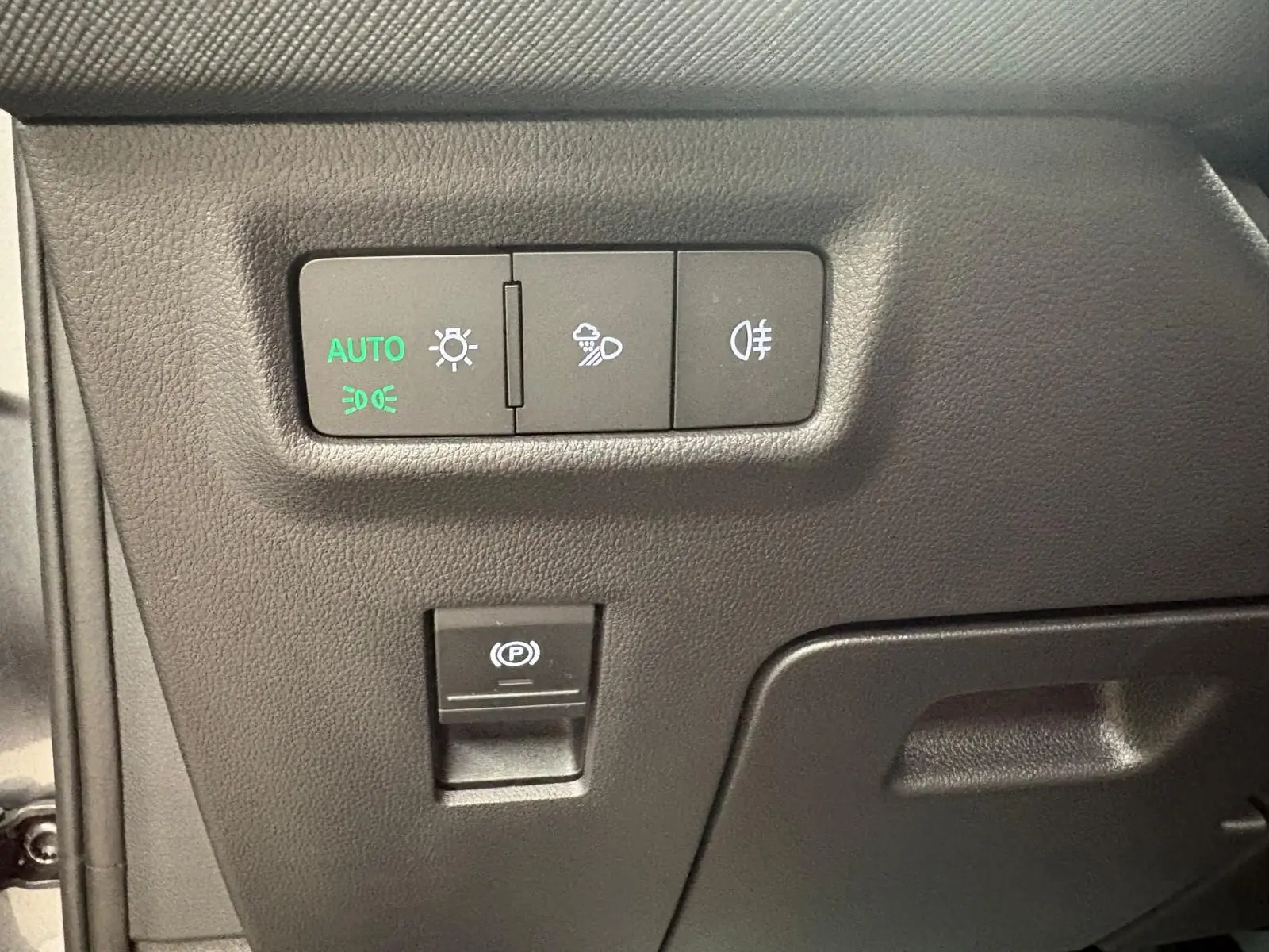 Gros plan sur les commandes d’éclairage et frein de stationnement électrique du Skoda Kodiaq gris graphite, intérieur côté conducteur.