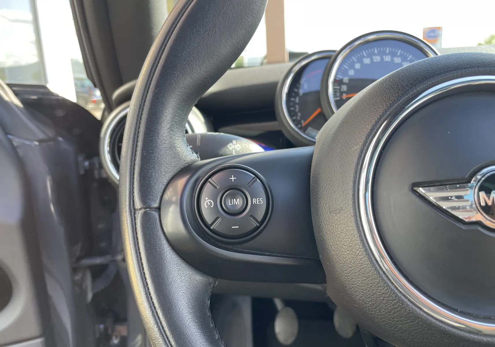 Gros plan sur le volant noir de la MINI F56 Cooper S 2015 avec commandes de régulateur de vitesse et tableau de bord visible.