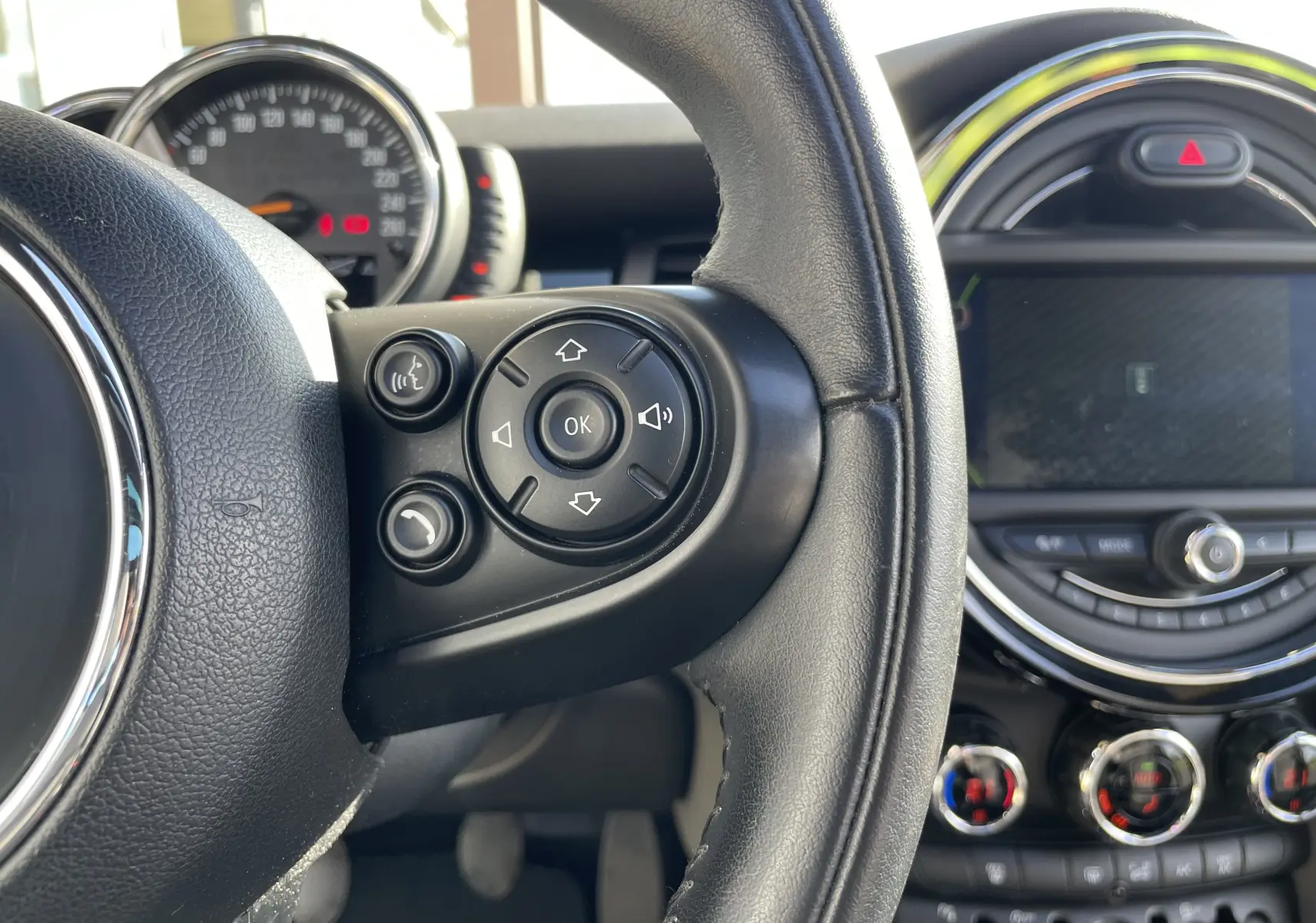 Gros plan sur le volant noir et les commandes multifonctions d'une MINI F56 Cooper S 2015, tableau de bord en arrière-plan.