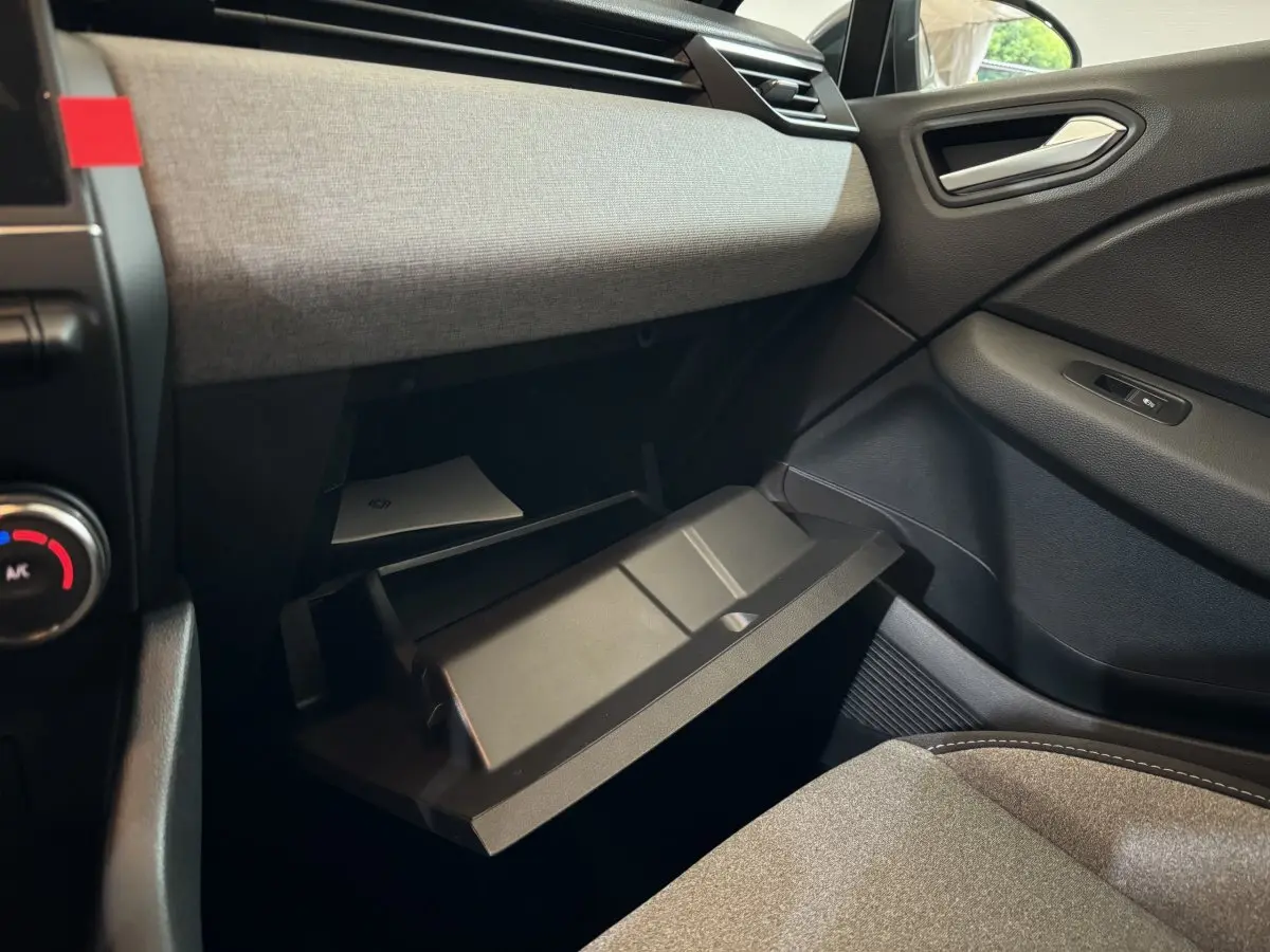 Intérieur de la Renault Clio 2025 gris clair, vue côté passager avec boîte à gants ouverte et tissu clair sur planche de bord.