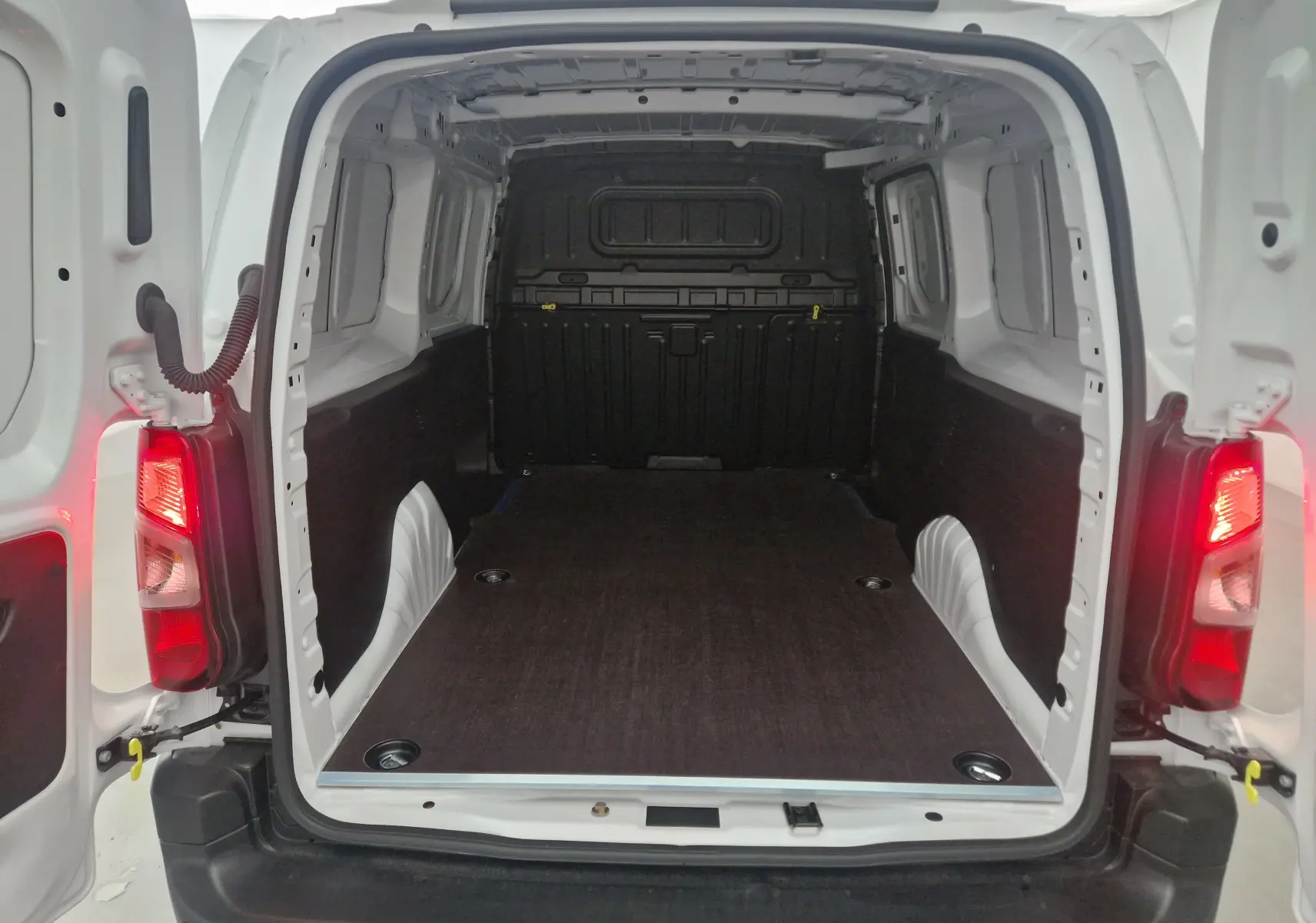 Vue arrière ouverte du Peugeot Partner blanc 2025 montrant l'espace de chargement avec plancher bois et parois protégées.