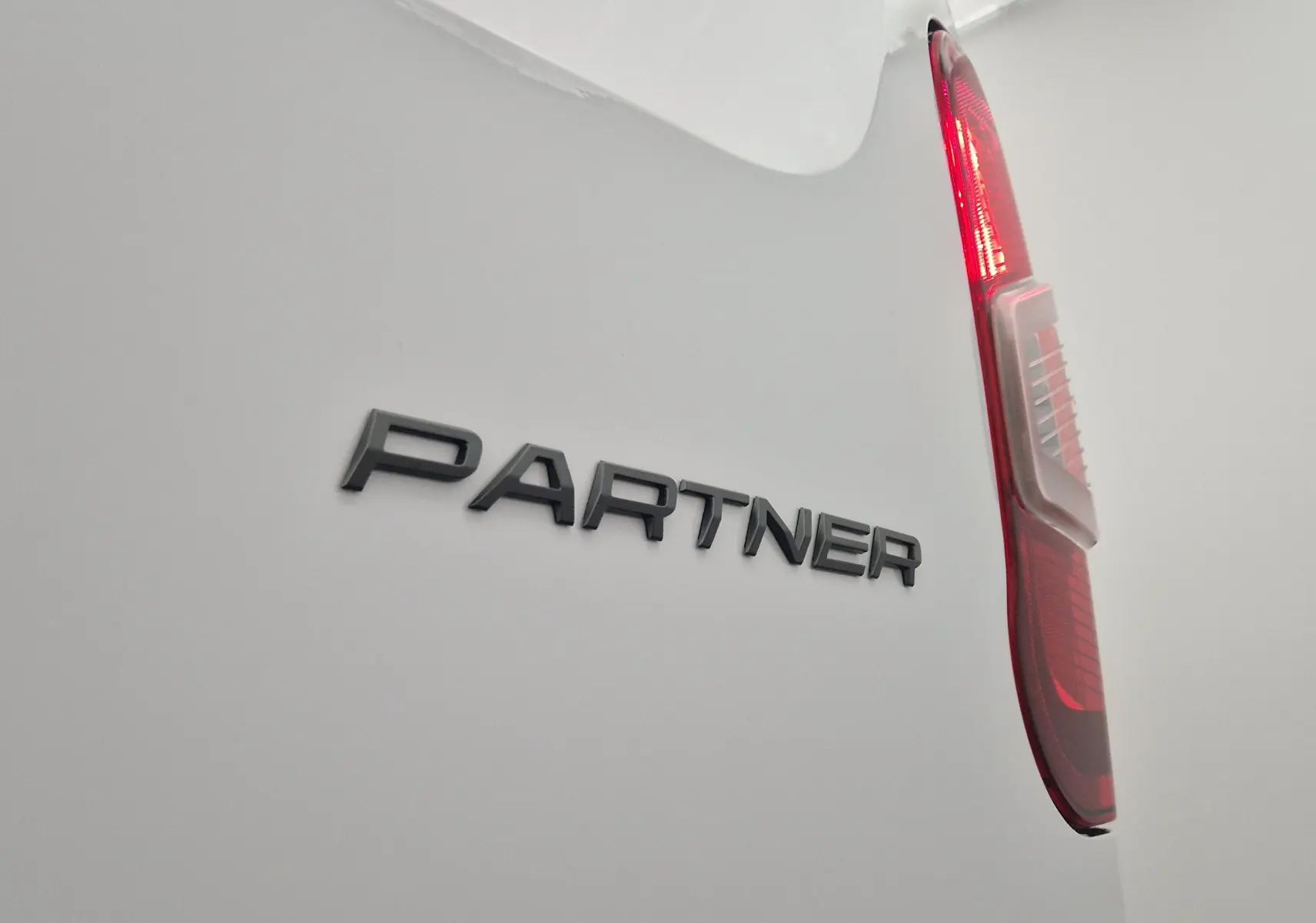 Gros plan sur l'arrière droit blanc du Peugeot Partner 2025, mettant en valeur le logo "PARTNER" et le feu arrière rouge.